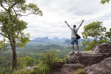 Traveler man standing on big stone holding his hand up and see landscape view at Dragon Crest mountain, popular landmark travel adventure in krabi thailand.