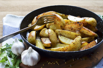 Closeup of fried potato wedges with dill, garlic and pepper, decorated in a rustic style. Rustic fried potatoes in a cast iron skillet at home.