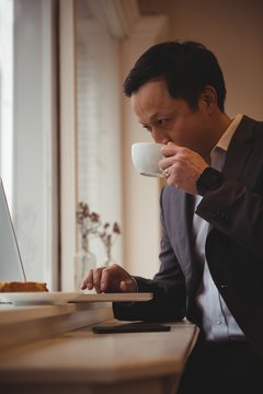 Businessman drinking coffee while using laptop