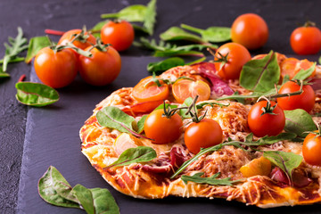 Homemade pizza with bacon, tomatoes, spinach, arugula and cheese