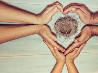 Strongly holding hands of a family making a heart sign on wooden background. Family bonds,...