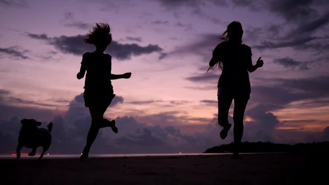 Pretty Young Girls Running with Dog at Beautiful Sunset on the Beach. HD Slowmotion. Phangan, Thailand.