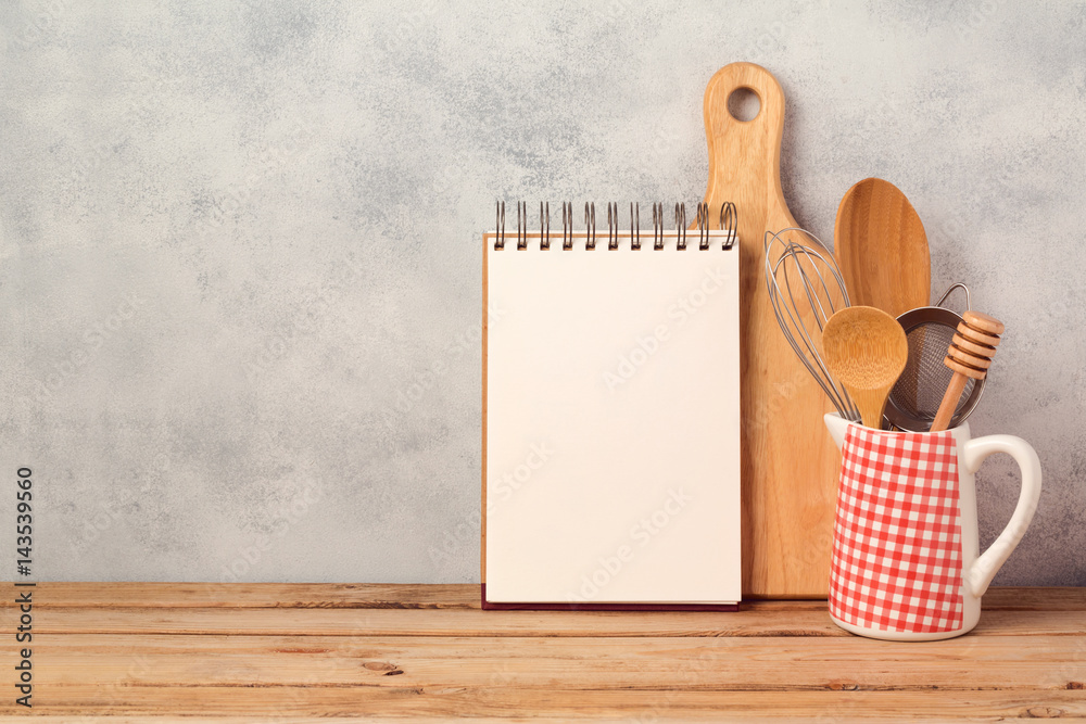 Wall mural blank notebook and kitchen utensils on wooden table over rustic background with copy space