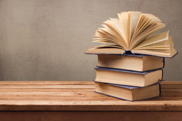 Open book and stack of old books on wooden table over rustic background