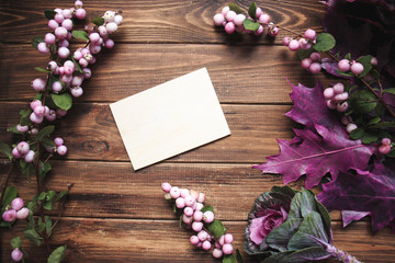 Blank greeting card with snowberry and purple leaves on the wooden background