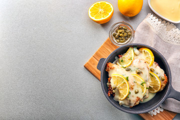 Frying pan with delicious chicken piccata on wooden board