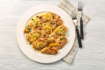 Plate with delicious chicken piccata on wooden table
