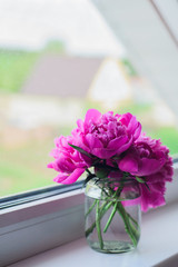 pink peonies bouquet in glass jar on white window sill on house background