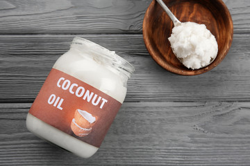 Spoon and glass jar with fresh coconut oil on grey wooden background