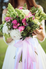 Elegance wedding bouquet of pink hydrangea and rose flowers with long silk ribbons in bride's hands.Close-up bunch of flowers. Bridal accessories in pink colors