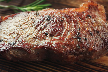 Delicious grilled steak with aromatic rosemary on wooden board, closeup