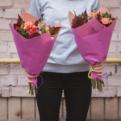 Young girl in a gray sweatshirt holding two beautiful bouquets in pink paper