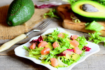 Salmon, avocado and lettuce salad. Homemade salad with slices of smoked salmon, fresh avocado and lettuce leaves mix on a plate. Avocado, fork on a wooden table. Closeup