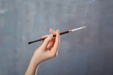 Female hand with cigarette holder on color background