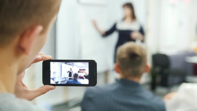 A man at business meeting shooting video by mobile phone, seminar or lecture