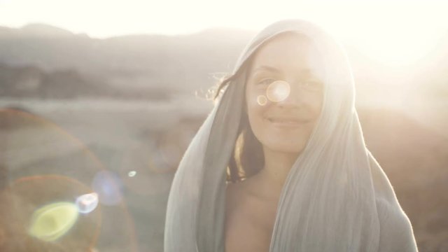 happy young woman standing in wind against a desert sunset landscape with a beautiful sun flare