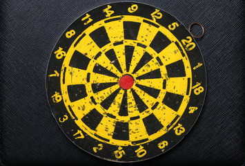 Used and vintage dartboard with a lot of damaged hole from arrow marked put on the black color leather surface as a background represent the entertainment game.