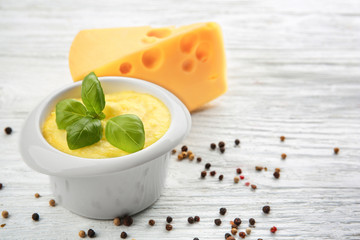 Bowl with cheese sauce, basil and spices on light wooden background