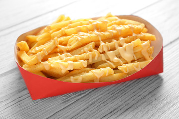 Paper red box full of delicious french fries with cheese sauce on white wooden background