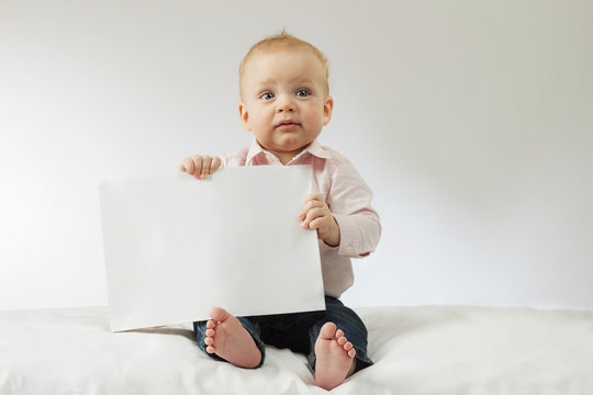 Baby boy holding white blank. Infant kid sitting with poster in his hands. Mock up. Copy space. Idea for postcard