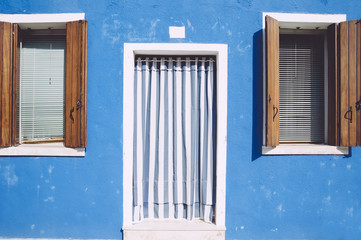 Beautiful colorful house facade on Burano island, north Italy. Colorful old blue wall with a door and wooden windows