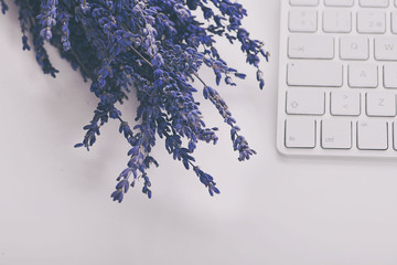 Lavender flower next to computer keyboard on white background.