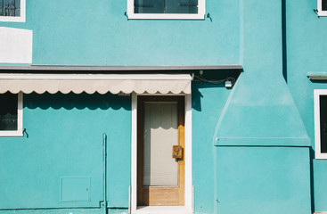 Beautiful colorful house facade on Burano island, north Italy. Mint green wall with an old door and two windows