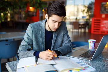 Shot of young male  student sitting at table and writing on notebook. Young male student studying...