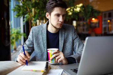 Shot of young male  student sitting at table and writing on notebook. Young male student studying in cafe 
