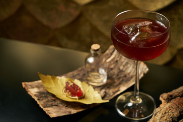 Fresh branded red alcoholic cocktail with a small bottle for alcohol and a red marmalade snack on a black stone bar counter.  Concept of alcoholic and non-alcoholic bar beverage.