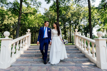 The bride and groom walking down the stairs in the park. The bridegroom embraces the bride. Wedding couple in love at wedding day