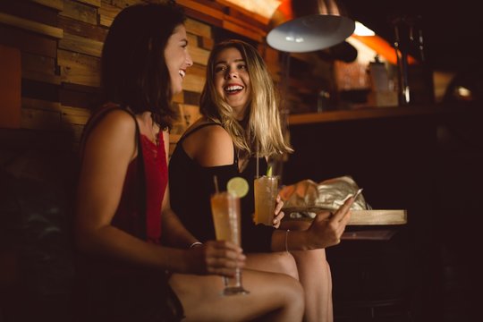 Beautiful women using mobile phone while having cocktail
