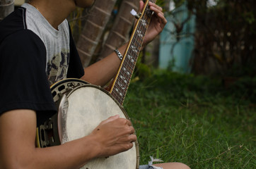 .Young man sitting banjo happily. Under the shade of trees on the lawn in the morning.