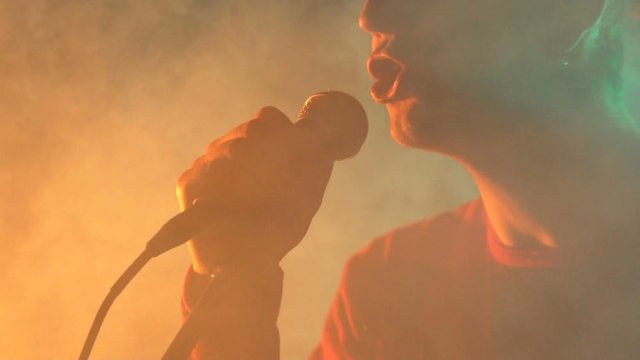 Hipster guy sings on stage in smoke. Slow motion.  Music, Sound, Band, Concept.