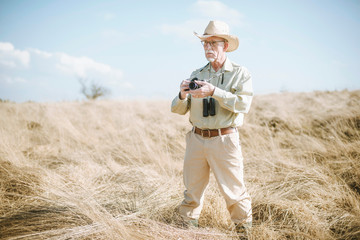 Senior safari man with camera and binocular in field.