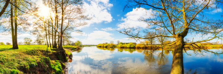 Panorama einer Landschaft im Frühling am Fluss mit Sonne, Wiesen und Bäumen
