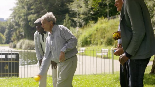  Happy senior male friends bowling & laughing together in the park