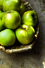 Green ripe organic apples, local produce, in rustic wicker basket on weathered wood table, harvest, autumn, cozy atmosphere