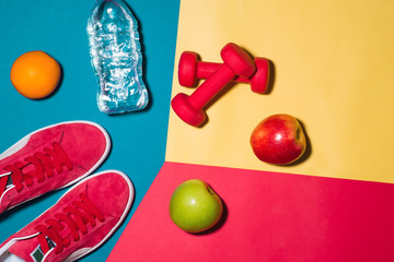 Sport concept. Fitness equipment. Sneakers, water, apple, dumbbell on colorful background. © makistock