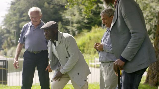  Happy senior male friends bowling & laughing together in the park