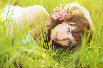 romantic woman with a mole on her cheek lying on the spring green grass looking at the camera bright pleasant light, delicate white dress, cosy photo