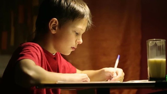 The boy at the desk writes in a notebook