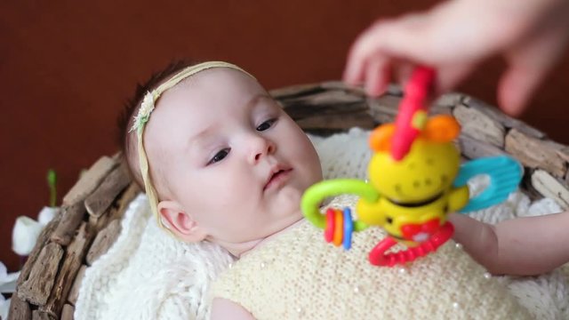 baby is lying in bed on the back in yellow knit clothes and show rattle toy