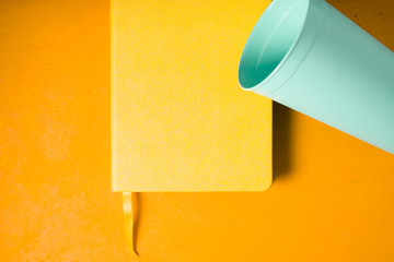 Blue plastic cup with notebook on the yellow background top view