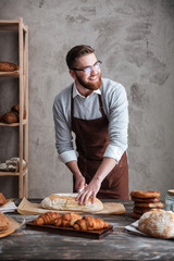 Happy young man baker standing at bakery cut the bread.