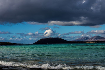 tre strisce colorate,
 nuvole nere, cielo azzurro e mare turchese