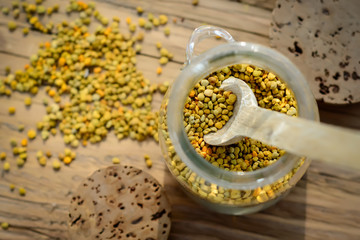 Grains of bee pollen in jar and wooden spoon on wooden table. Apitherapy. Bee products.