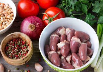 Raw chicken hearts, with tomatoes and herbs on a wooden table.