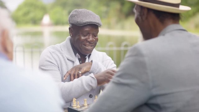  Portrait smiling senior man playing chess in the park with a friend