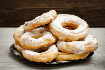Donuts sprinkled with powdered sugar, dark wood background. Close-up, side view